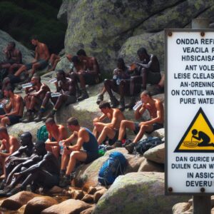A photography of hikers near the Onda refuge on the GR20 trail in Corsica, drinking water with a visible caution sign about water safety.
